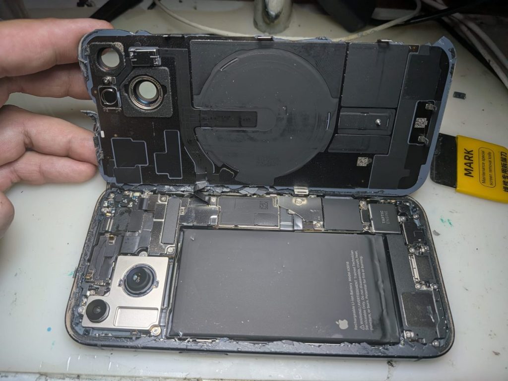 iPhone 15 con la tapa trasera abierta durante el cambio de cristal trasero