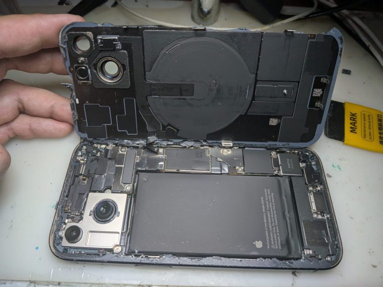 iPhone 15 con la tapa trasera abierta durante el cambio de cristal trasero